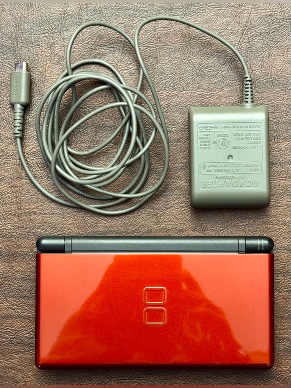 Nintendo DS Lite Dual-Screen Handheld Console in bright orange with Gray Charger